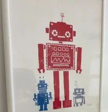 Gerahmter Druck mit einem großen roten und zwei kleinen blauen Robotern in der Werkstatt