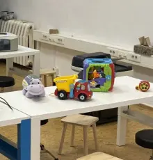 Ausgediente Elektro-Spielzeuge auf dem Werkstatttisch: ein Spielzeuglaster, ein Lernspielzeug und ein Plüschtier